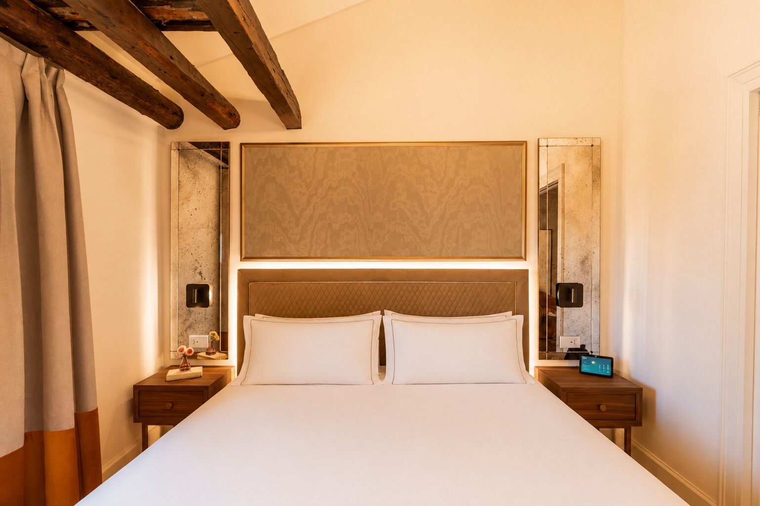 Een hotelkamer met een groot bed, houten hoofdeinde, nachtkastjes met lampen en een spiegel.