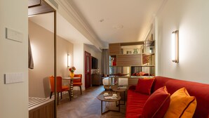 A hotel room with a red sofa, a dining area with a table and chairs, a kitchen area, and a hallway leading to another room. - Hotel San Samuele (Venice)