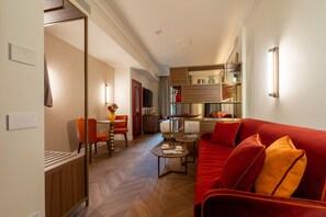 A hotel room with a red sofa, a dining area with a table and chairs, a kitchen area, and a hallway leading to another room. - Hotel San Samuele (Venice)