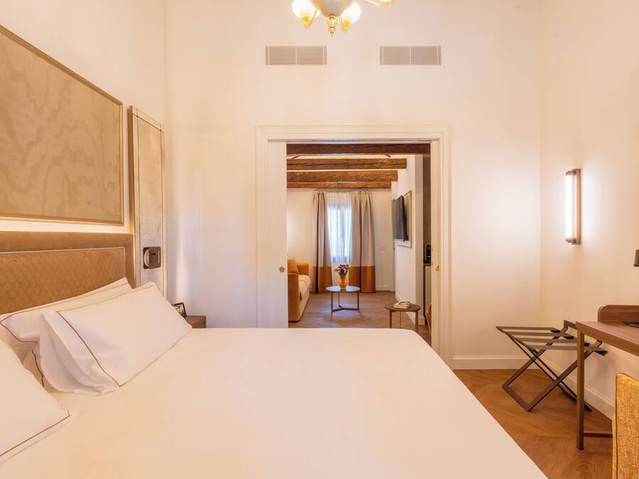 A hotel room with a large bed, a desk with a chair, a television, and a bathroom visible through an open door.