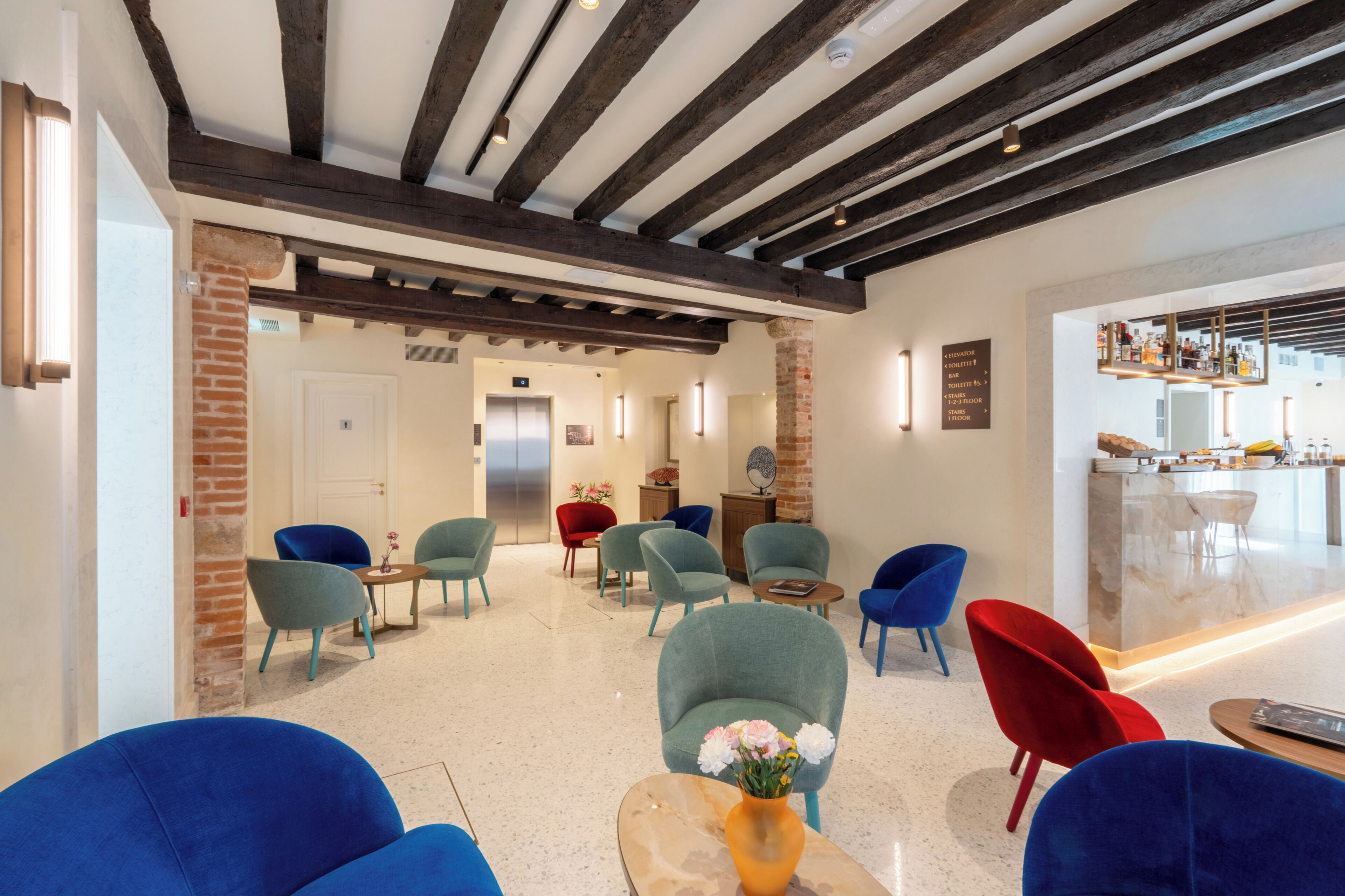 Un hall d'hôtel doté d'un bar, d'un espace salon avec un vase de fleurs et d'un ascenseur moderne.
