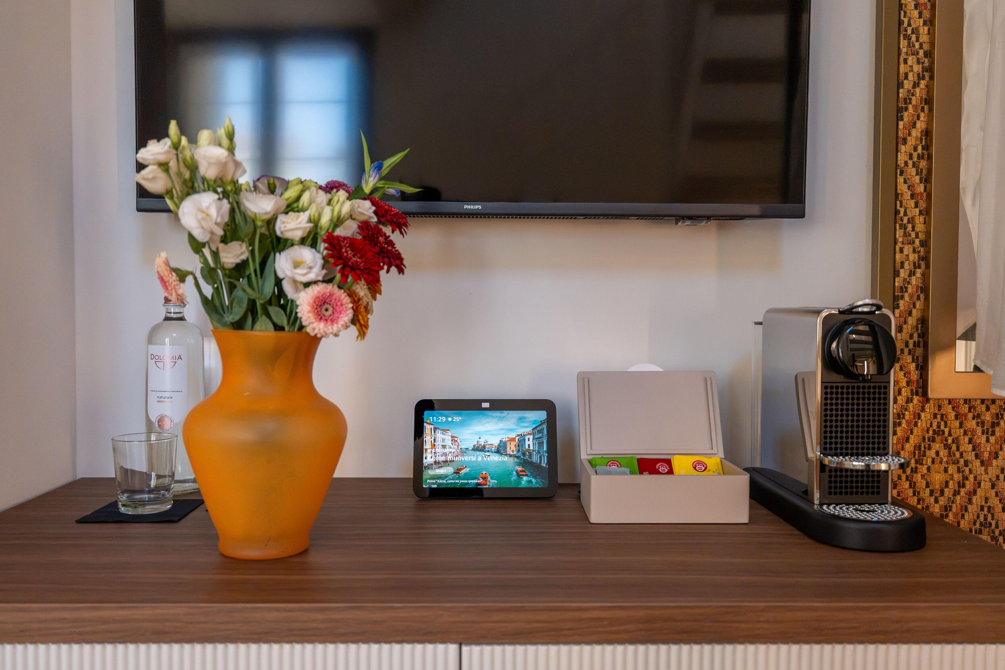 Una mesa de madera con un florero, una botella, una tableta, una caja y una máquina de café.