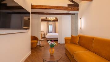 Ein modernes Hotelzimmer mit einer Couch, einem runden Couchtisch mit einer Vase, einem Fernseher und einem Bett mit Blick auf einen Balkon.