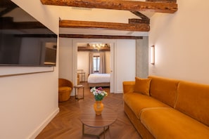 A modern hotel room with a sofa, a round coffee table with a vase, a TV, and a bed with a view to a balcony. - Hotel San Samuele (Venice)