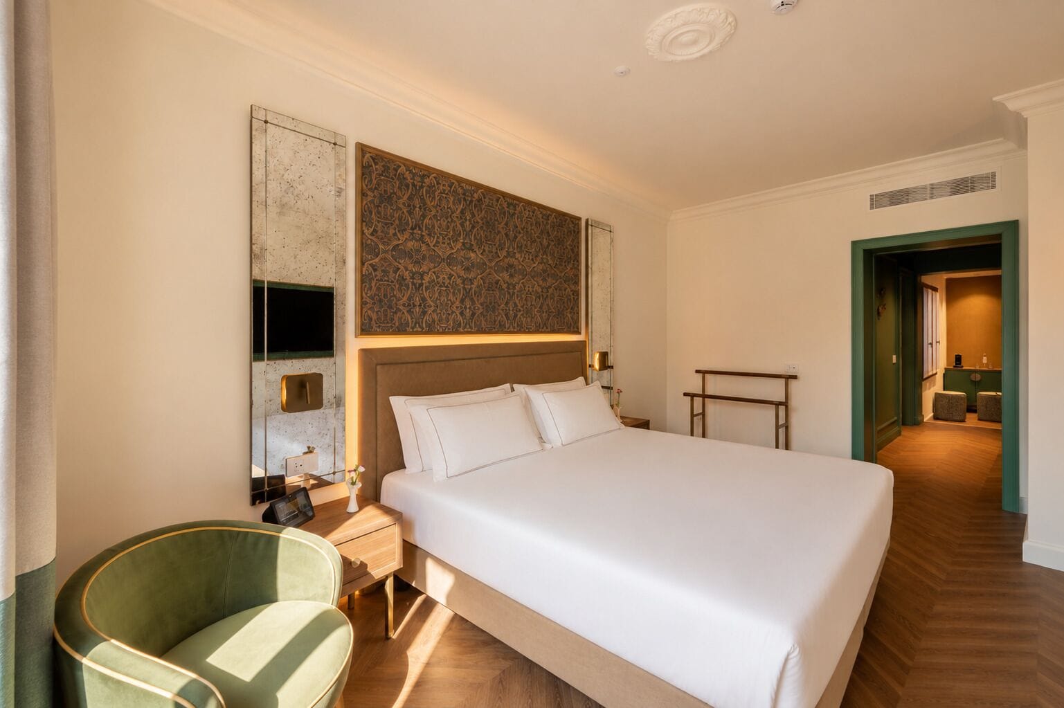 A hotel room with a large bed, a bedside table, a chair, and a decorative wall piece.
