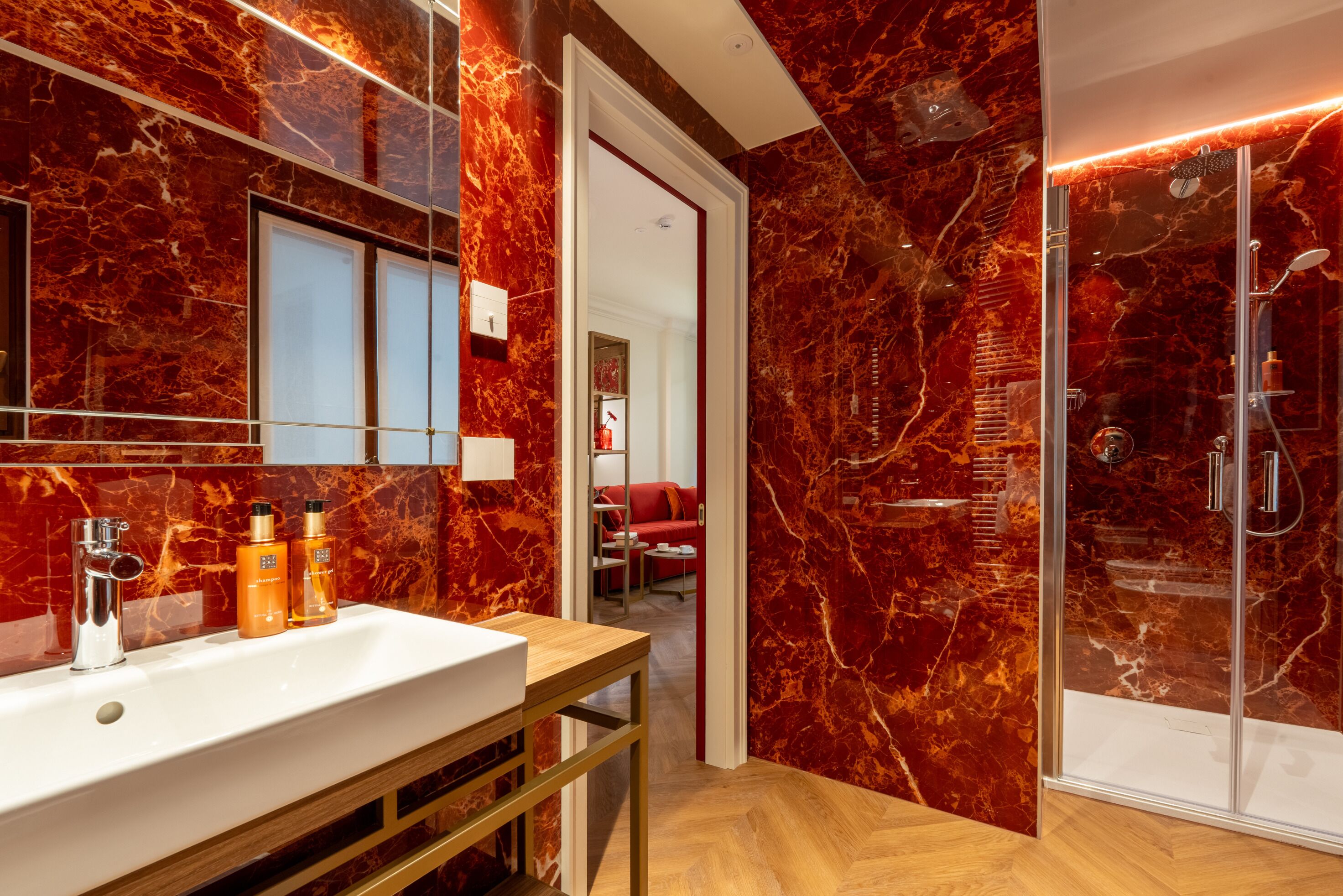 Un baño moderno con pared de mármol, lavamanos blanco y cabina de ducha de vidrio.