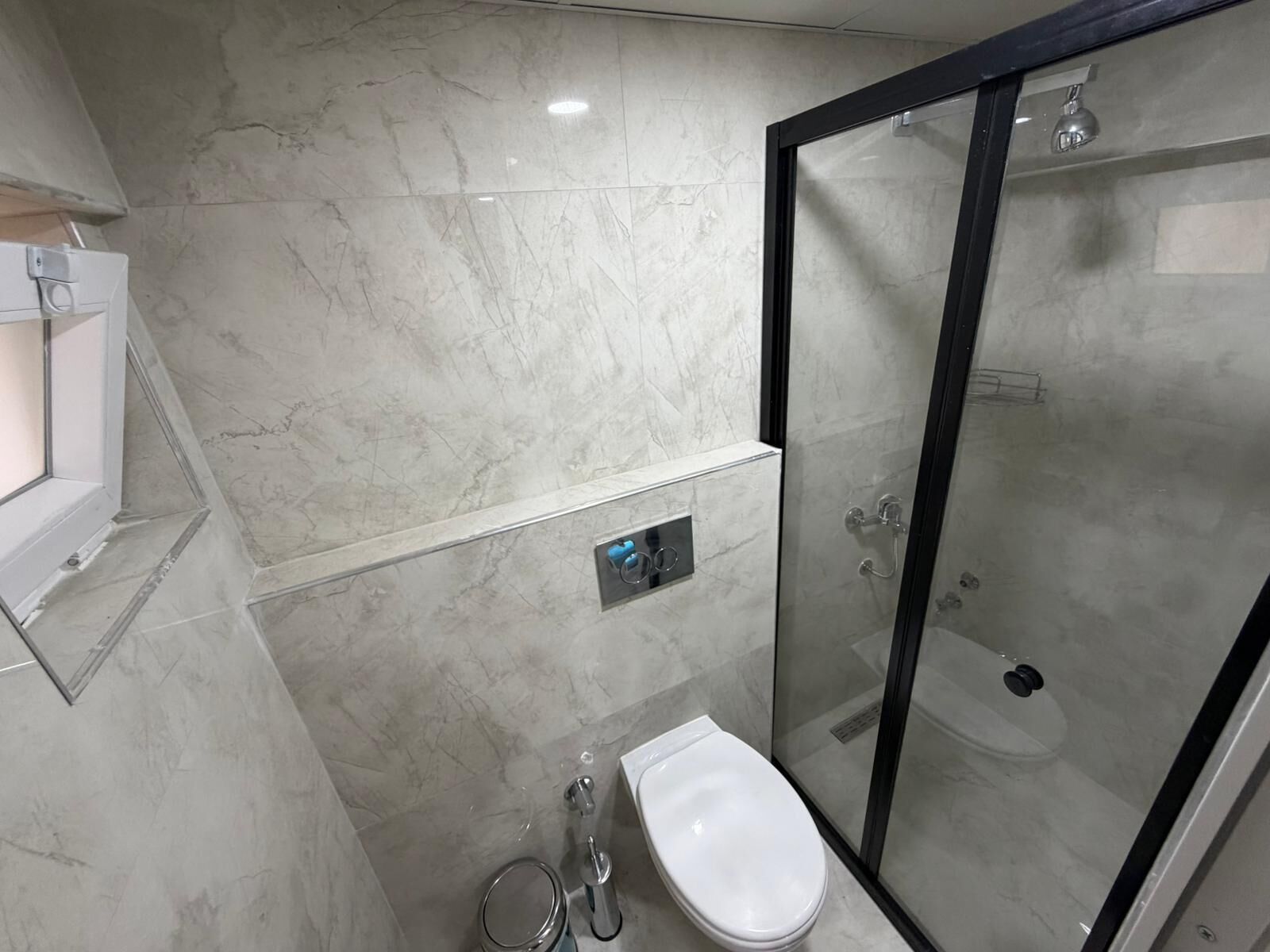 Une salle de bain moderne avec une douche à parois de verre, des toilettes blanches et un mur recouvert de carreaux de marbre.