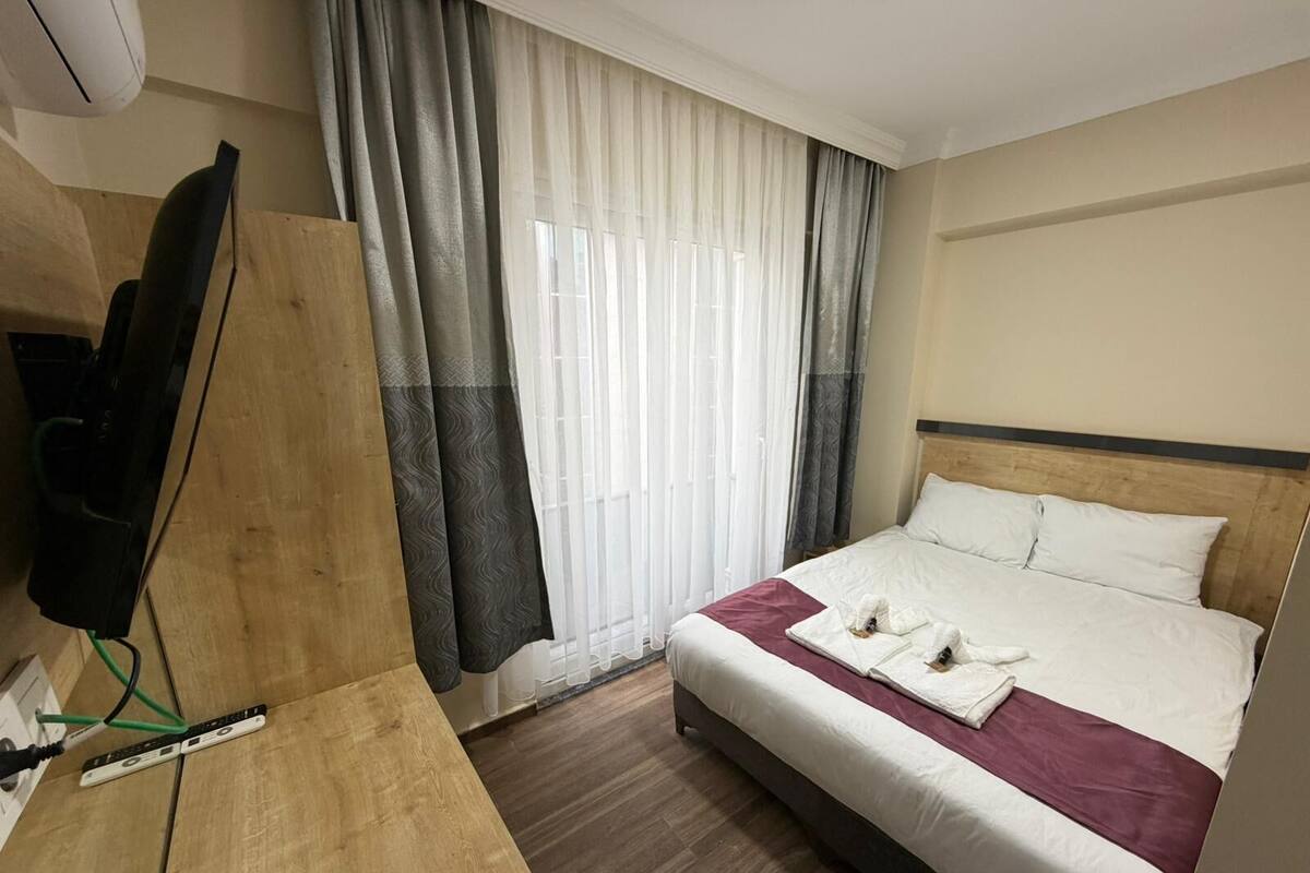 Ein Hotelzimmer mit einem Bett, einem Holztisch, einem Fernseher und einem Fenster mit Vorhängen.