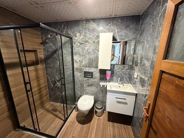 Un baño moderno con cabina de ducha de vidrio, inodoro, lavabo con espejo y mueble de madera.