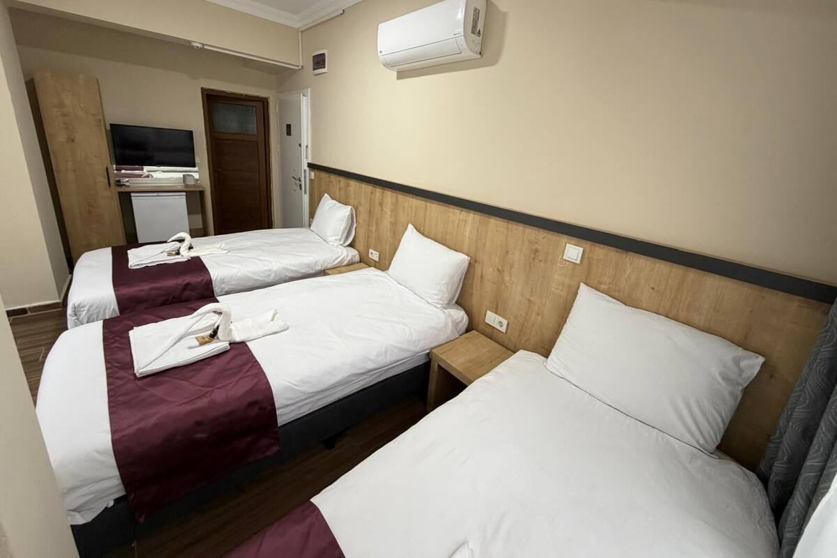 Ein Hotelzimmer mit drei Einzelbetten, einem Fernseher und einer Klimaanlage.