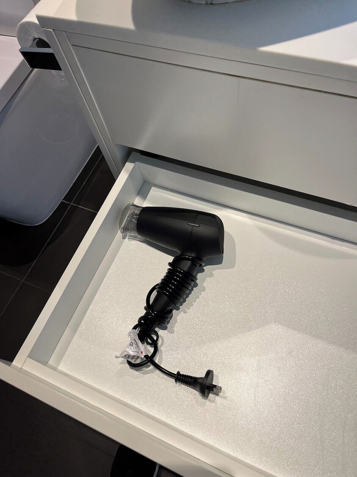 A hair dryer in a drawer with a power cord and a plug.