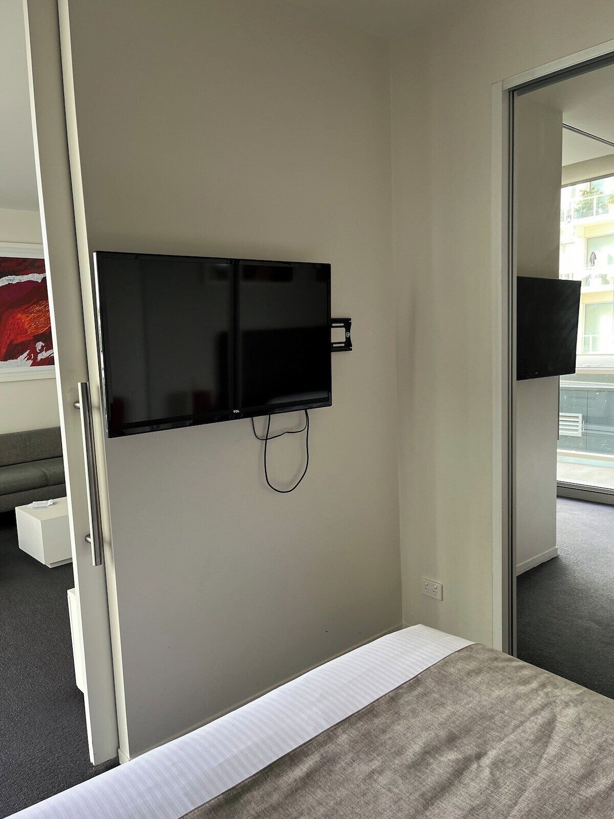 A hotel room with a bed, a flat-screen TV mounted on the wall, and a window providing a view of the outside.
