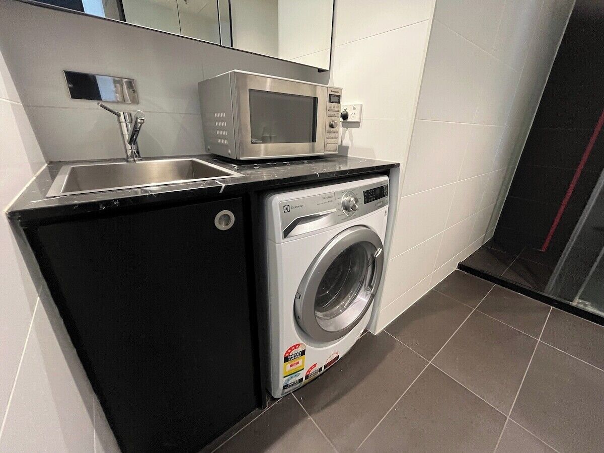 A compact kitchen with a microwave, sink, and washing machine.