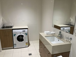 A modern bathroom with a washing machine, sink, and mirror. - Tasha's Apartments on Morphett (Adelaide)