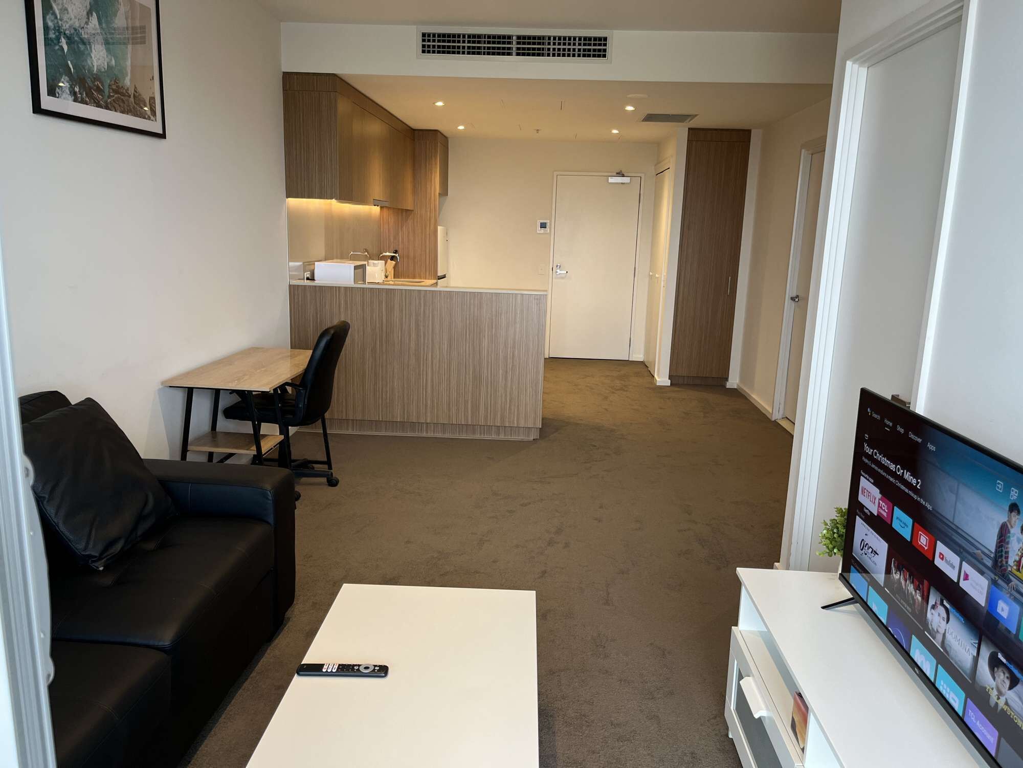 Een moderne woonkamer met een bank, een salontafel, een televisie en een keuken op de achtergrond.