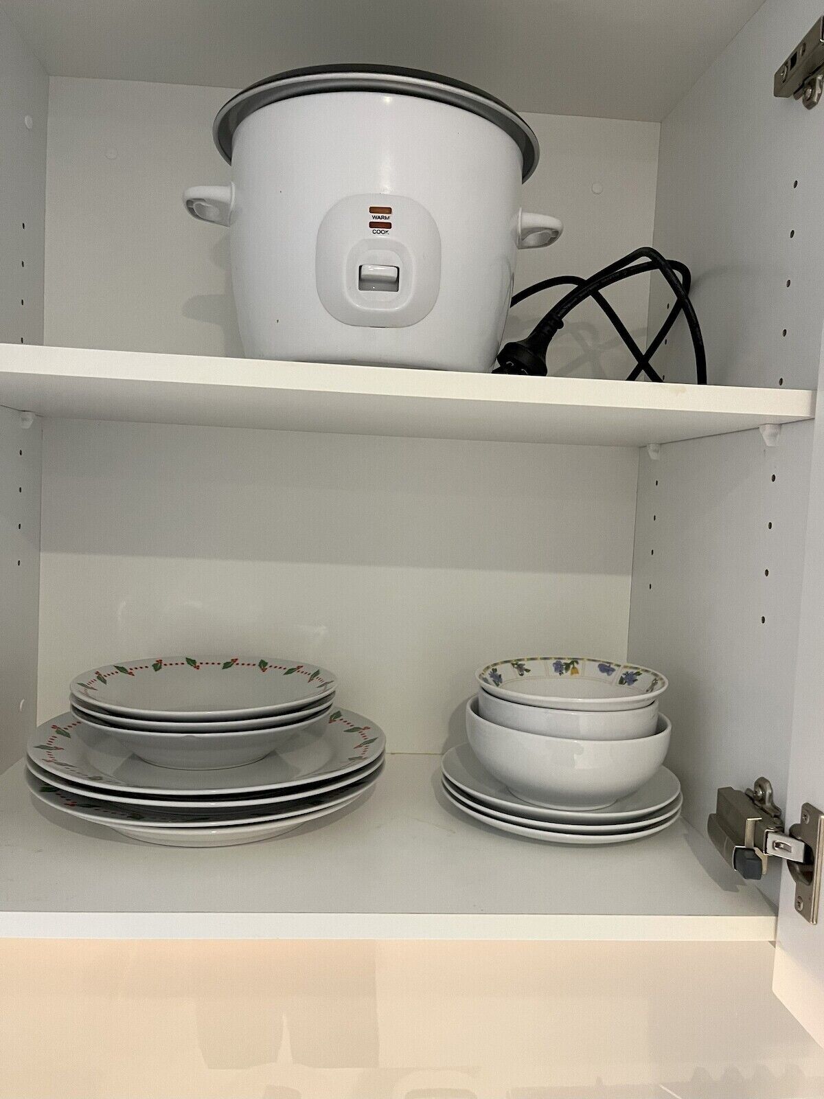 Una cocina con una olla de cocción lenta blanca en el estante superior y platos y recipientes apilados en el inferior.