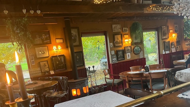 A cozy restaurant interior with wooden tables, chairs, and a central wood-burning stove. - Natuur Vakantie Bonte Haan - Het Heerhuys (Berg en Terblijt)
