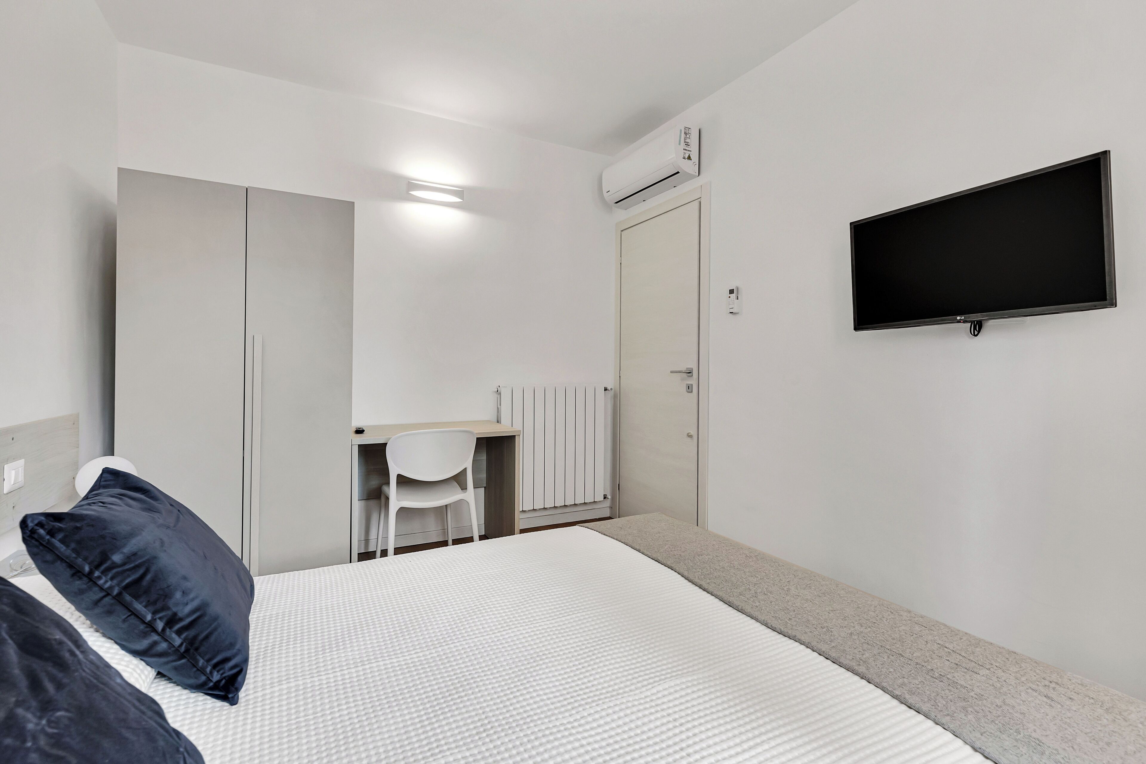 A bedroom with a bed, a desk, and a TV.