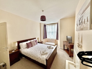 A hotel room with a bed, bedside tables, a television, and a window with curtains. - Tides Reach Filey, Sleeps 13,dog friendly, close to beach,town, park and pubs. (Filey)