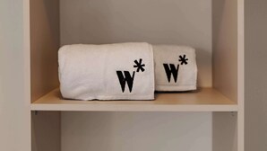 Ein Regal mit zwei weißen Handtüchern, jedes mit einer schwarzen Stickerei, einem 'W' und einem Sternchen.