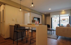 A modern kitchen with a bar area, bar stools, and a dining table with chairs. There are two bottles on the counter and a refrigerator in the background. - w Tranquil 2BR w Balcony in Miraflores (Lima)