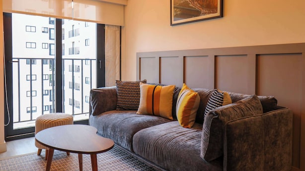 A modern living room with a grey sofa, a round wooden table, and a large window offering a view of a building. - w Marvelous 2BR With Balcony in Miraflores (Lima)