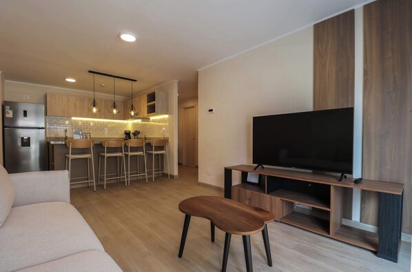 Een moderne woonkamer met een bank, een houten bankje en een televisie op een houten dressoir.