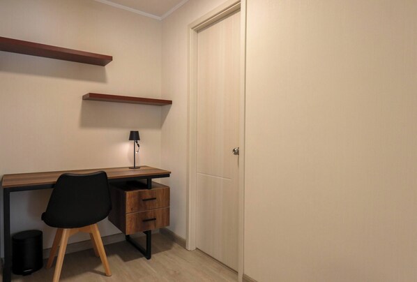 A small, neatly organized room with a wooden desk, a black chair, a lamp, and a closed door. - w Exquisite 2BR w Balcony in Miraflores (Lima)