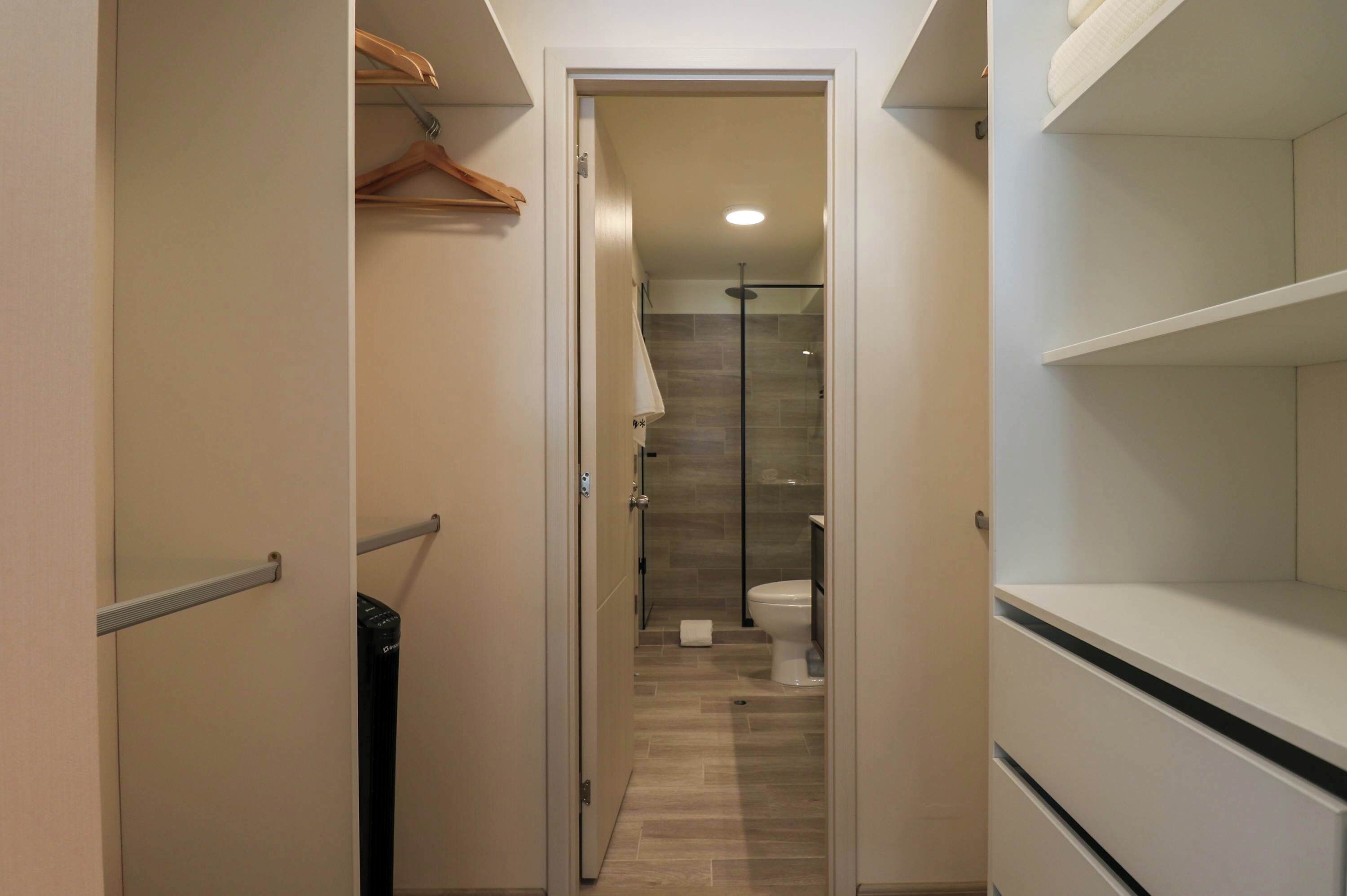 A narrow hallway with a door leading to a bathroom. The bathroom has a shower, toilet, and a towel rack.