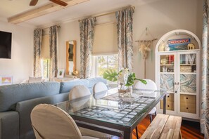 A living room with a glass-top coffee table, a sofa, and a cabinet with glass doors. - Under the Palms - Relaxing Condo Shared Pool Parking (Key West)