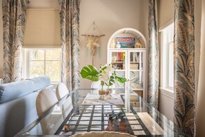 A living room with a glass coffee table, a sofa, and a bookshelf with a Monopoly game. - Under the Palms - Relaxing Condo Shared Pool Parking (Key West)