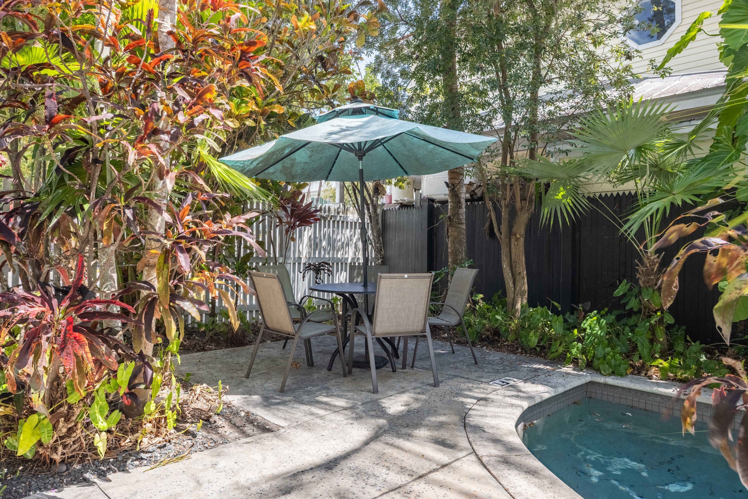 A patio with a table and chairs, surrounded by tropical plants and a small pool.