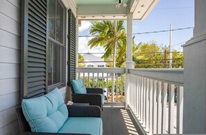 A covered porch with wicker furniture and a view of a palm tree. - Under the Palms - Relaxing Condo Shared Pool Parking (Key West)