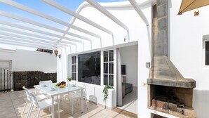 Une terrasse avec une table et des chaises en verre, un mur en pierre et une cheminée intégrée.