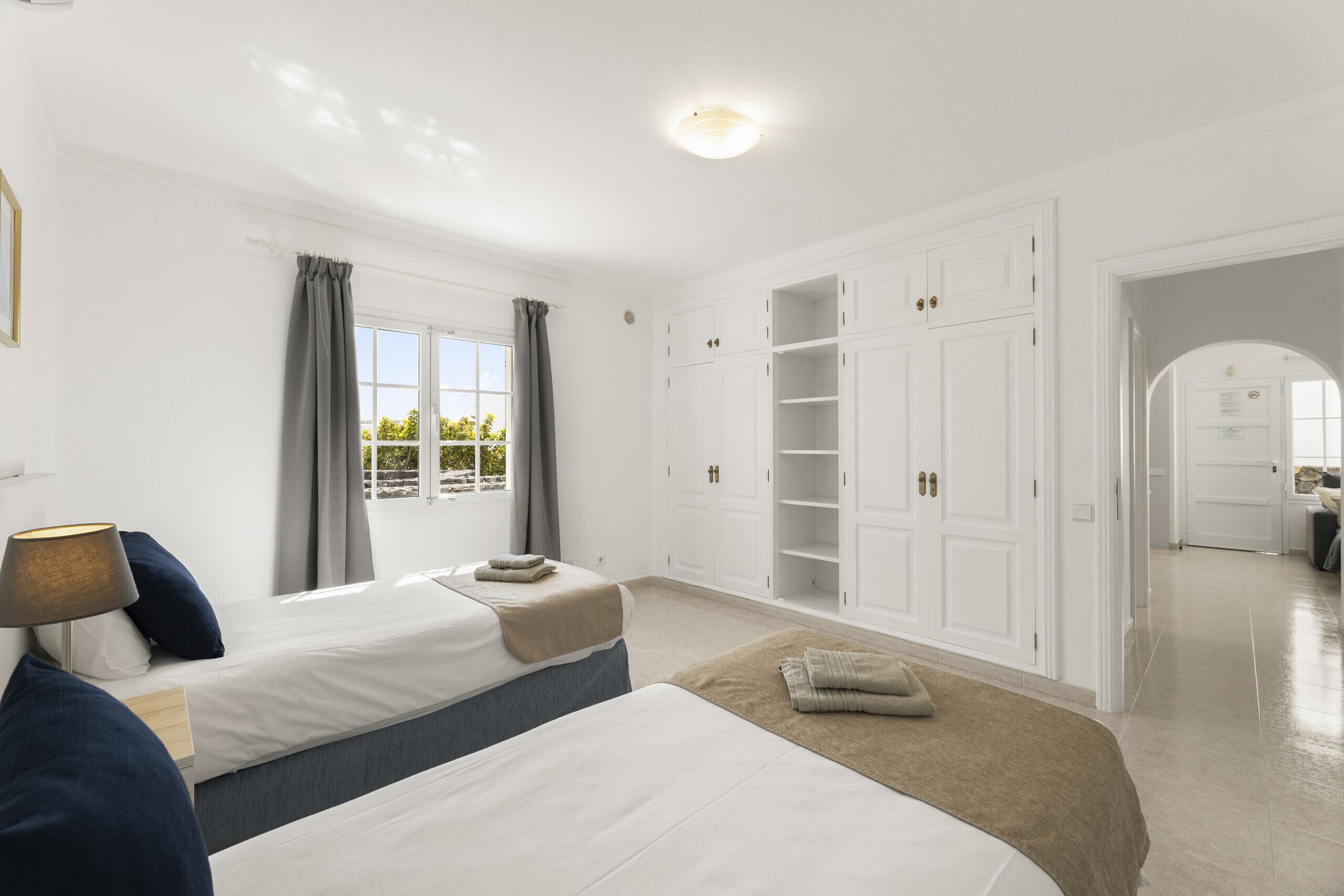 Habitación de hotel con dos camas, un armario, una ventana con cortinas y una lámpara.