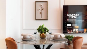 A dining area with a round table, two chairs, a vase with a plant, and a framed artwork on the wall. - Luxury Studio with Pool - Azizi Vista (Dubai)