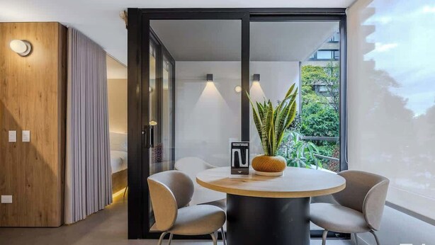 A modern dining area with a round table, two chairs, a potted plant, and a wooden cabinet. - NOK Stylish 1BR With Cozy Terrace (Bogotá)