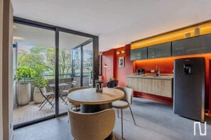 A modern kitchen with a black refrigerator, a dining area with a round table and chairs, and a glass door leading to an outdoor balcony with potted plants. - NOK 1BR Loft With Private Stylish Balcony (Bogotá)