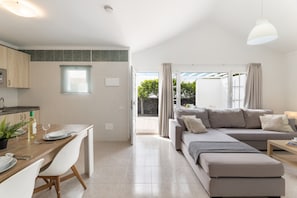 A modern living room with a sofa, a dining table with chairs, and a kitchen area with a window.