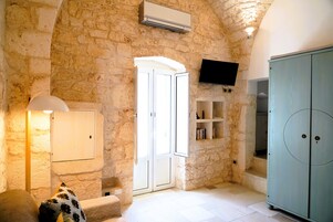 A stone-walled room with a white door, a television mounted on the wall, a cabinet, and a lamp.