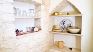 A kitchen with stone walls, shelves with glassware, plates, and a coffee pot. - Dimora Dolce Vista - Arcuève (Ostuni)