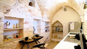 A compact kitchen with stone walls, a small dining area, and a refrigerator. - Dimora Dolce Vista - Arcuève (Ostuni)