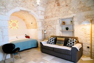 A room with a bed, a sofa, a chair, and a shelf with decorative items.