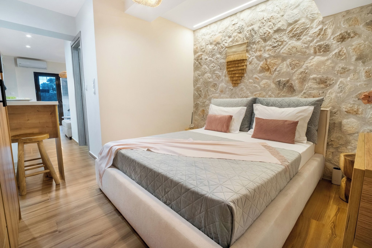 A bedroom with a stone wall, a bed with a quilted headboard, and a wooden nightstand.