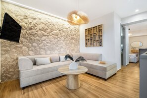 Una sala de estar moderna con una pared de piedra, un sofá gris, una mesa de centro redonda de madera y una lámpara colgante.