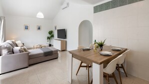 Un salon moderne avec un canapé, une table à manger pour deux personnes et un téléviseur fixé au mur.
