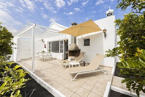 Eine Terrasse mit Grill, Liegestühlen und einer Pergola.