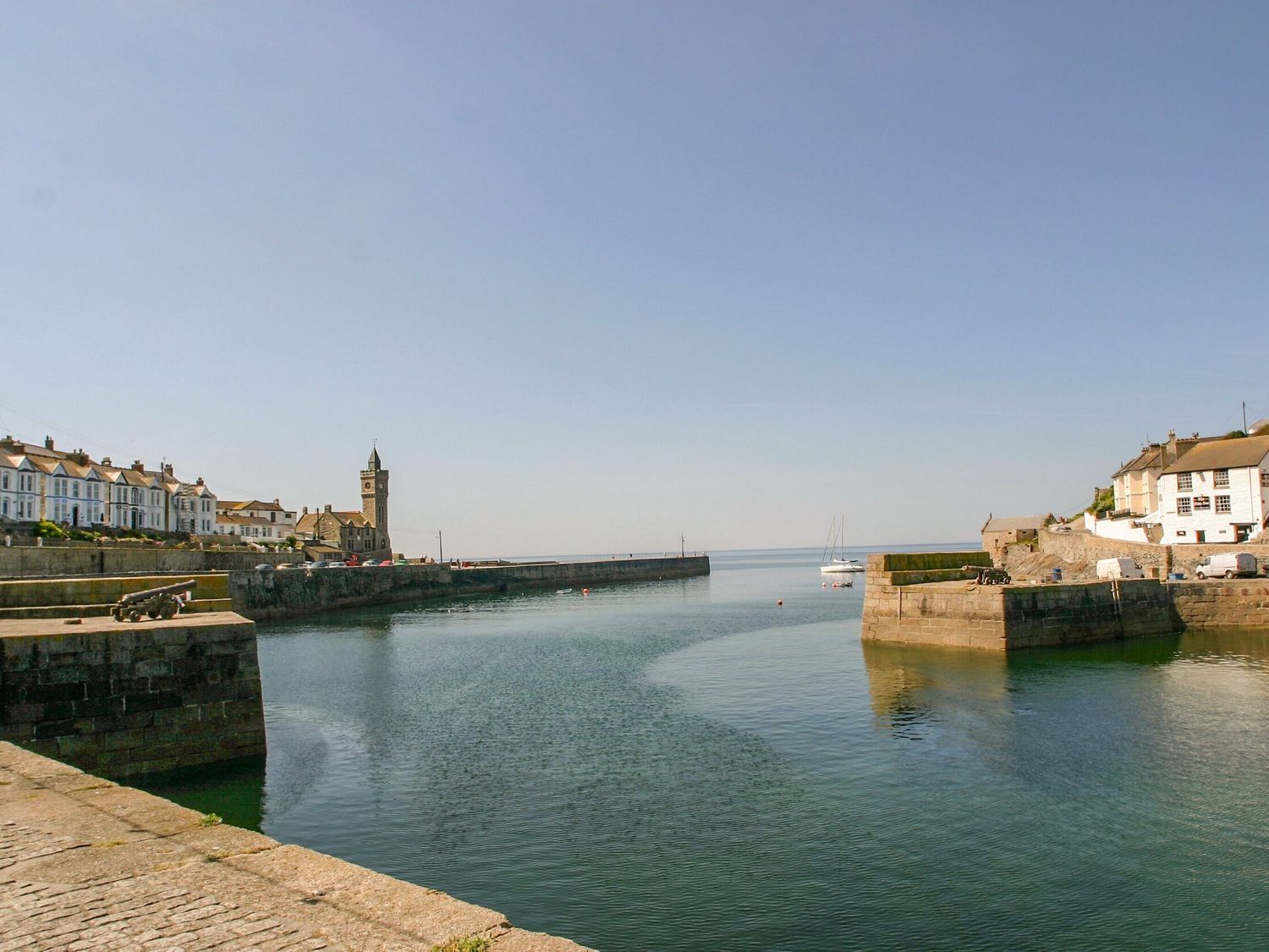 Un pueblo costero con un puerto tranquilo, muros de piedra y edificios tradicionales.