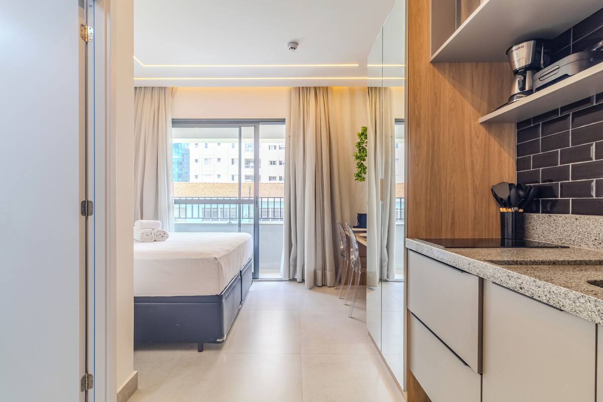Una habitación de hotel moderna con cama, kitchenette y vista a la ciudad.