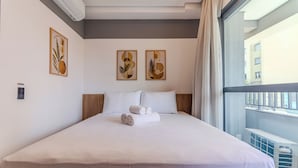 Hotellihuone, jossa on suuri sänky, valkoiset vuodevaatteet ja kaksi seinälle ripustettua taideteosta.